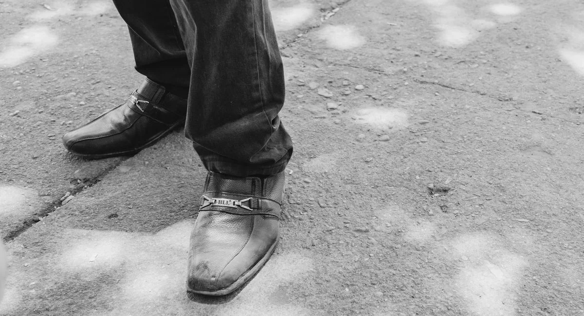 Monochrome close-up of leather shoes on a textured pavement, depicting casual fashion style.