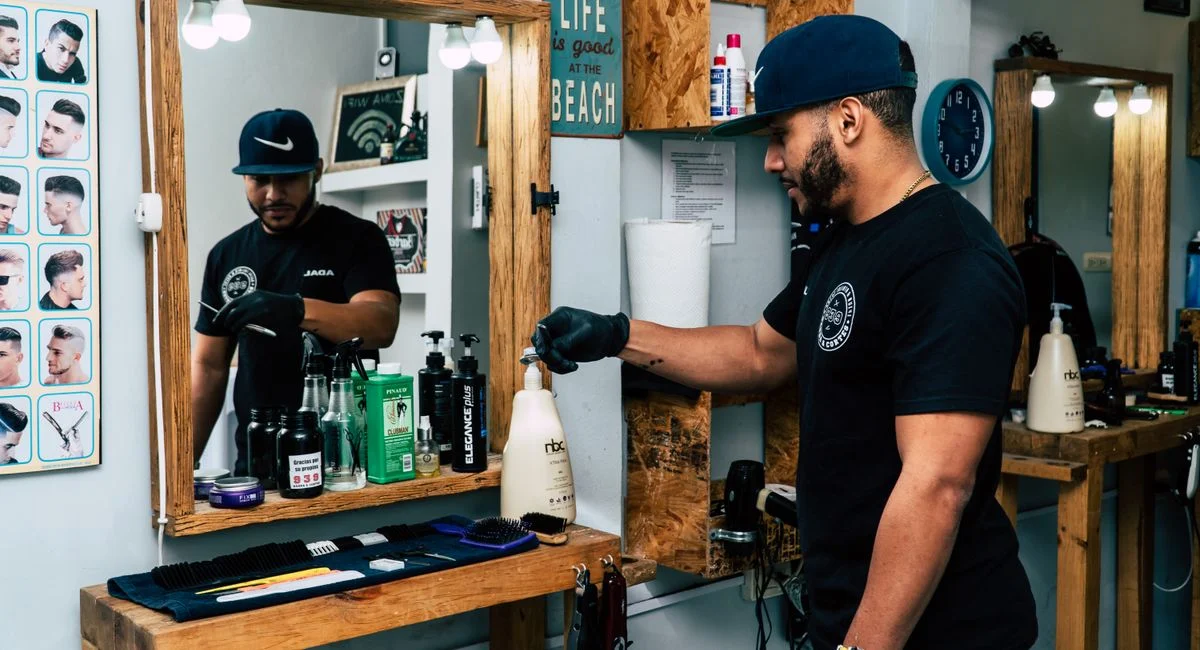 A barber in a stylish shop preparing tools for a haircut. Modern interior design with mirrors and grooming products.