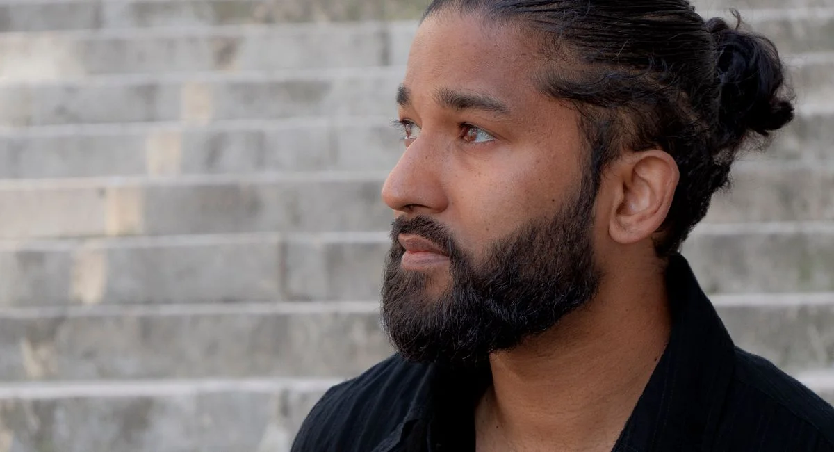 Profile of a bearded man with a bun looking thoughtful on stone steps.