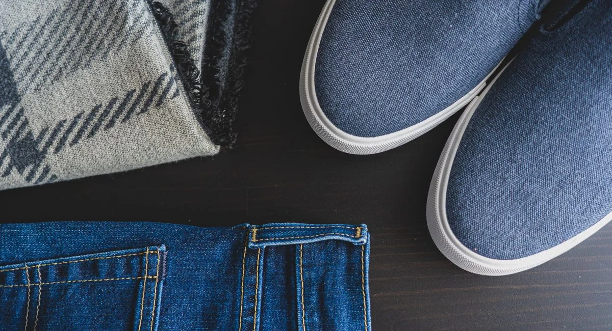 Flat lay of denim jeans, blue sneakers, and a plaid scarf for a casual look.