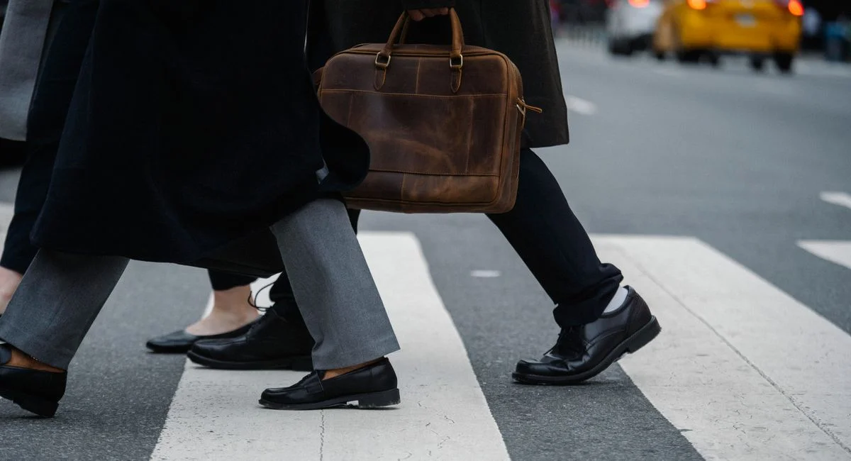 Side view of crop unrecognizable coworkers in formal wear with leather briefcase crossing urban road