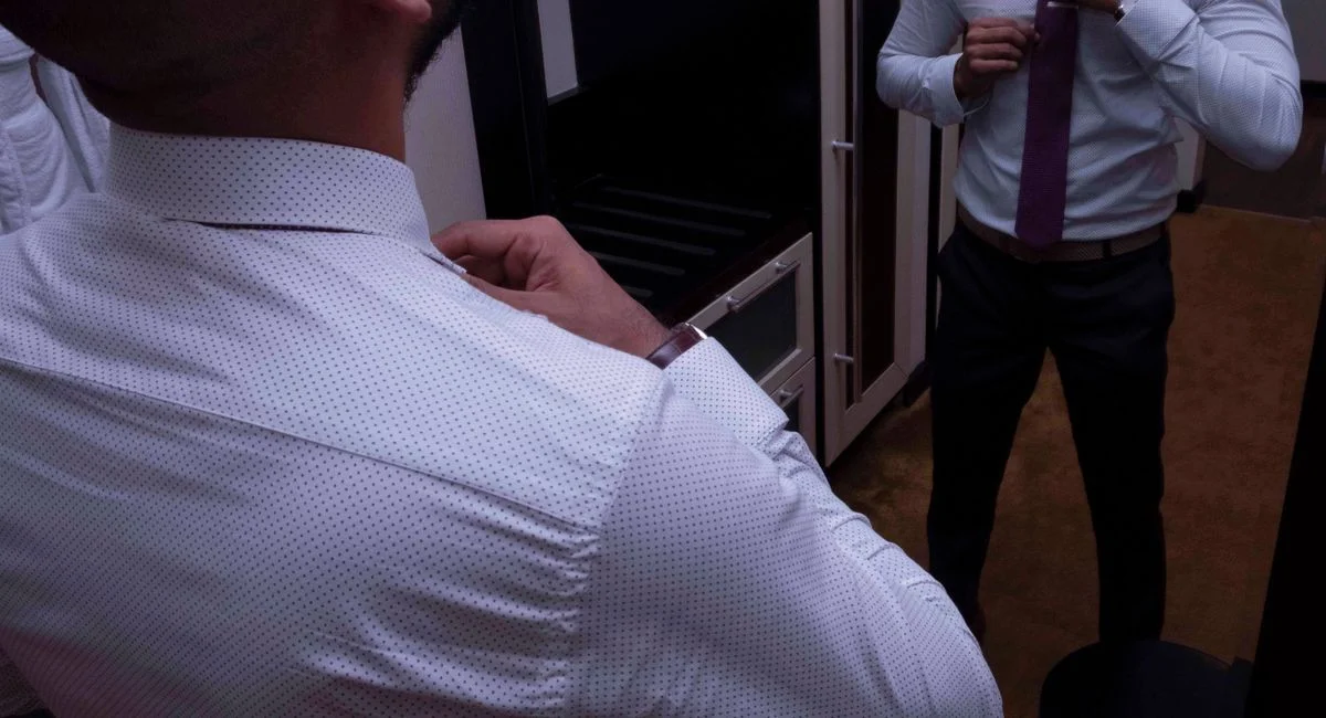 Professional man adjusting necktie in front of a mirror, showcasing style and elegance.