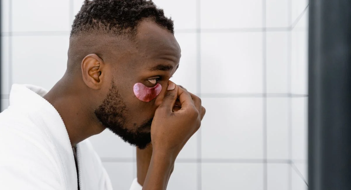 Side view of a man applying under eye mask, focusing on skincare routine.
