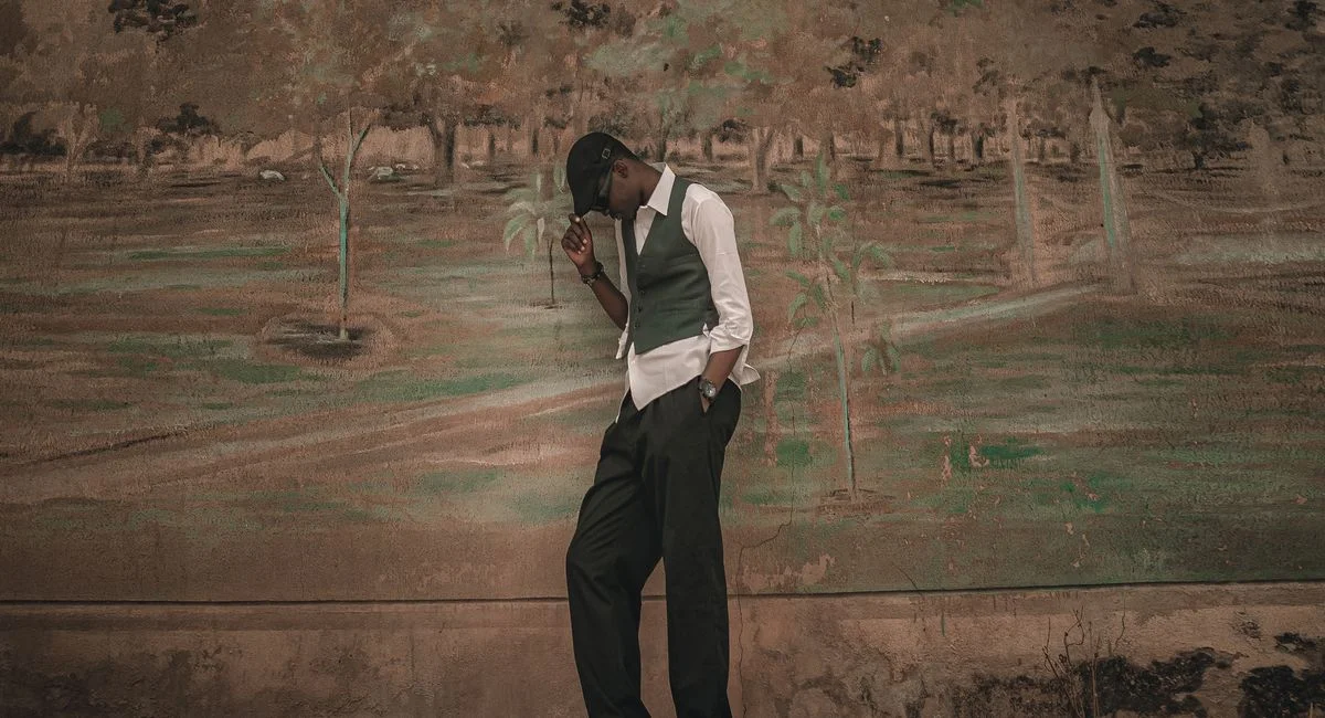 Artistic photograph of a stylish man posing in front of a detailed wall mural outdoors.