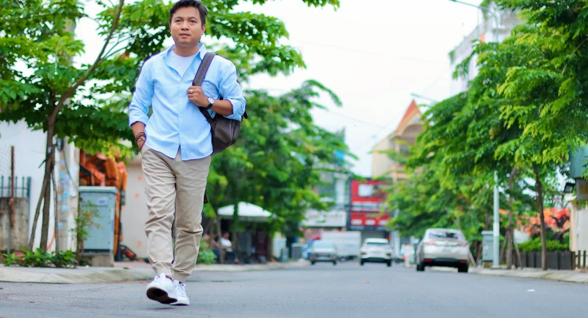 Man walking on a quiet city street on a sunny day with green trees.