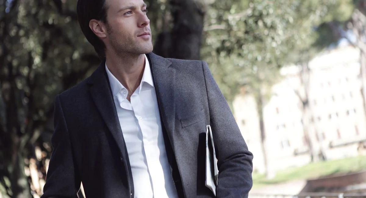 Elegant young man in formal attire standing outdoors, exuding confidence.
