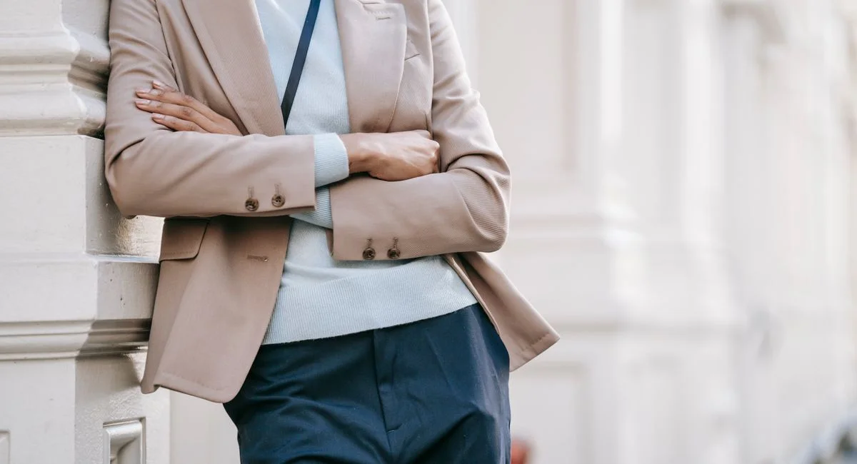 Crop anonymous stylish female manager in smart casual outfit leaning on elegant building wall with folded arms while standing