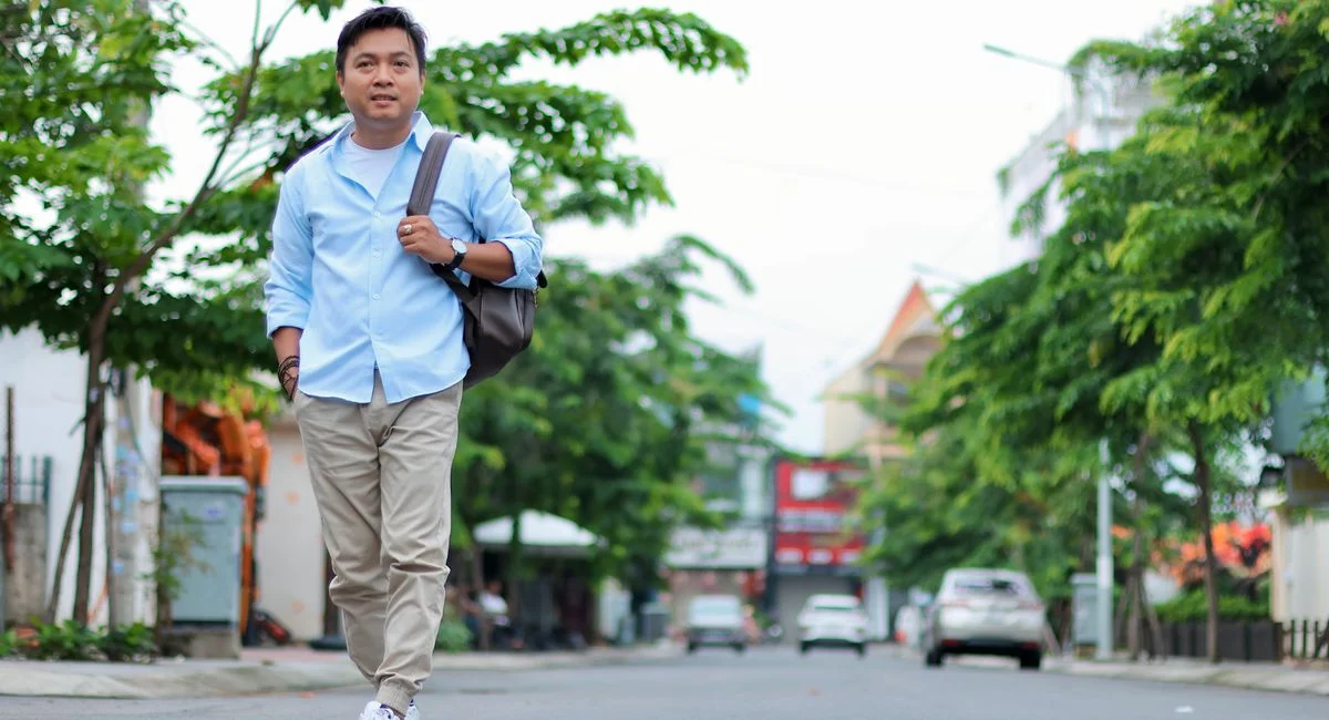 Man in casual attire walking confidently on a sunny city street.